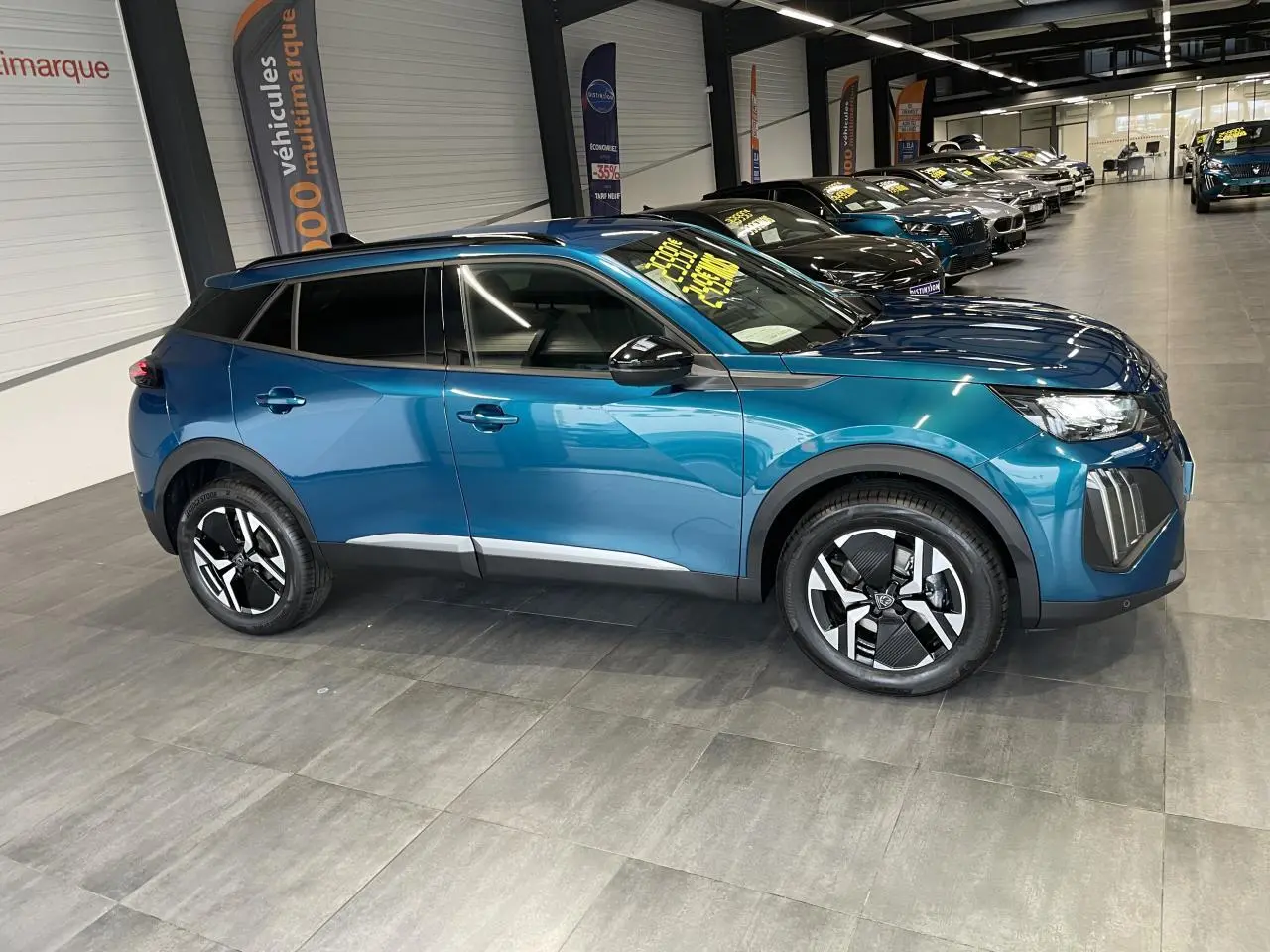 Peugeot 2008 hybride bleu en vue profil droit dans un showroom, avec jantes alliage bi-ton et barres de toit noires.