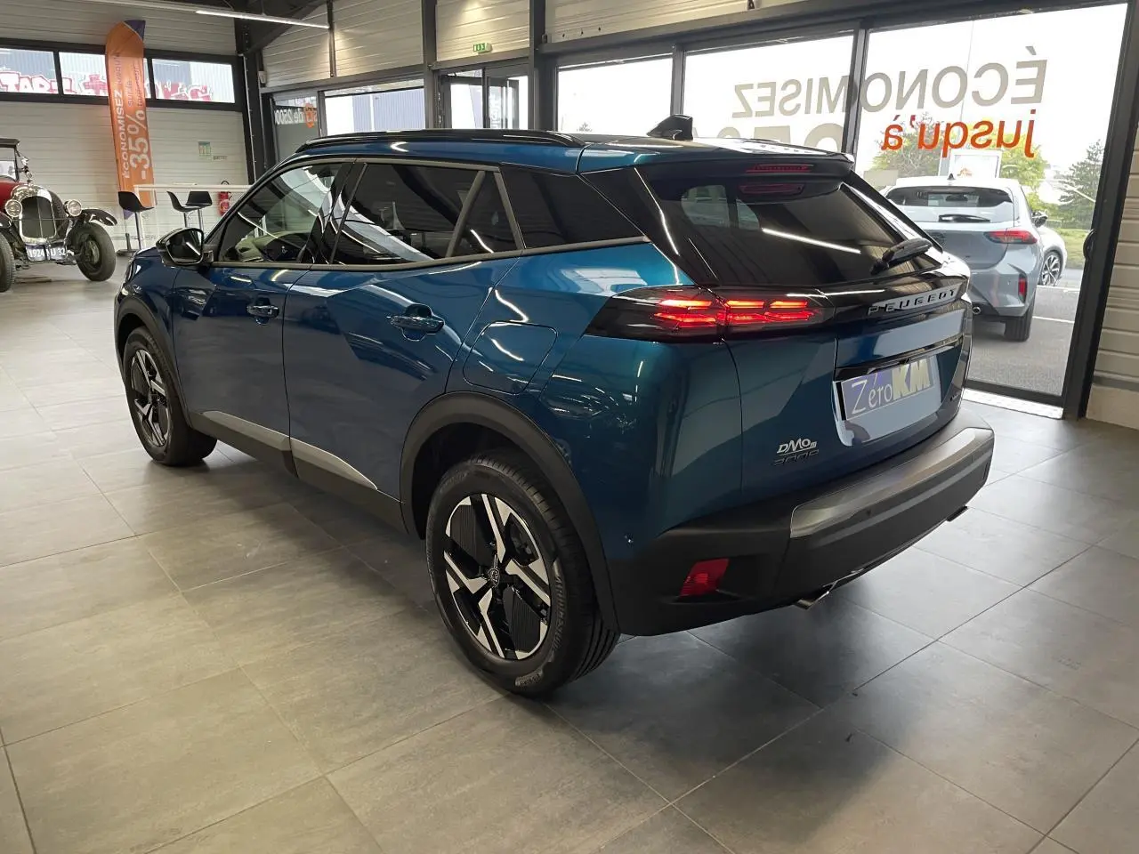 Vue 3/4 arrière droite d'un Peugeot 2008 bleu métallisé avec toit noir et jantes alliage bi-ton en showroom.