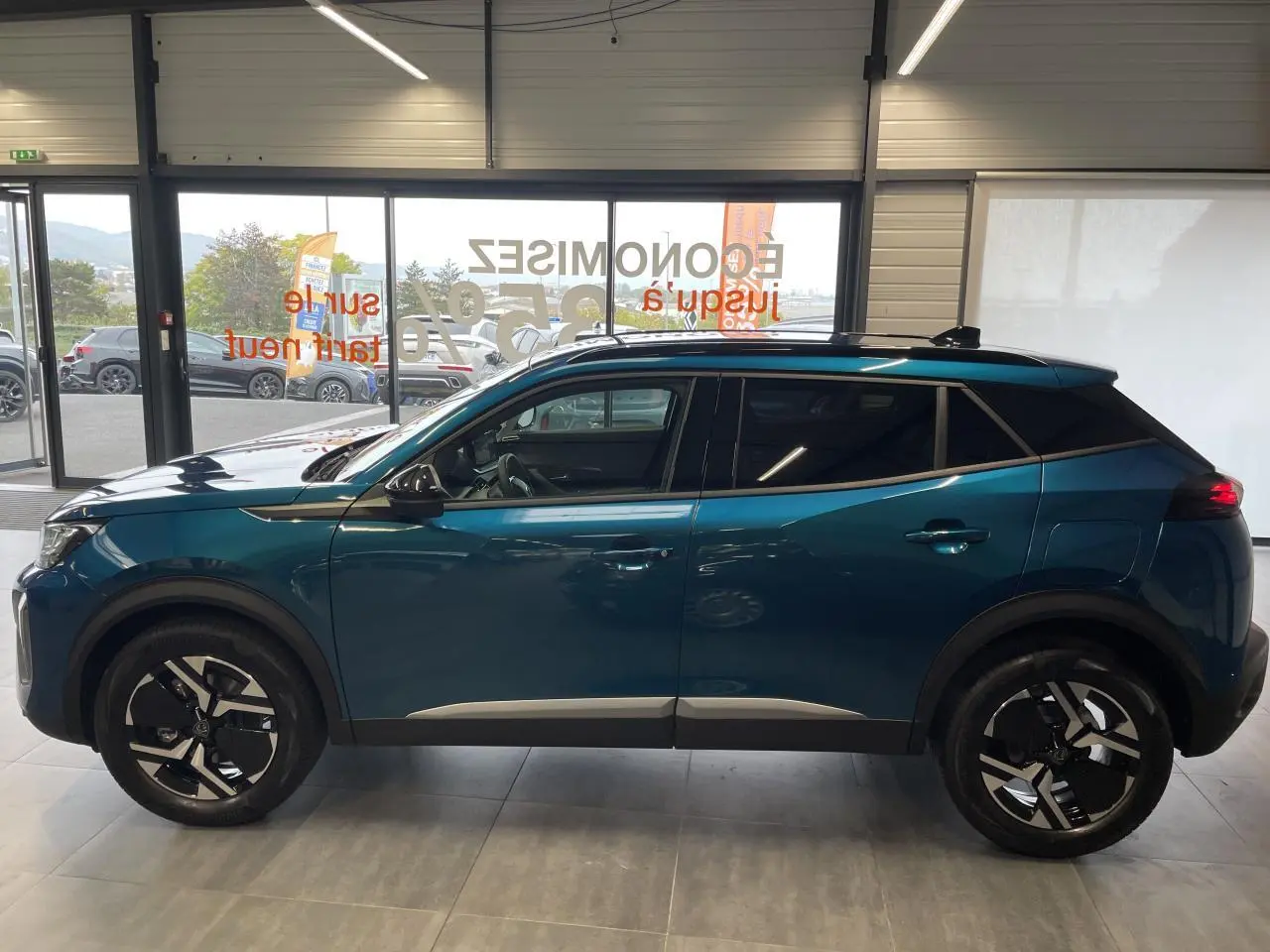 Profil côté gauche du Peugeot 2008 hybride bleu avec jantes alliage 17'' bi-ton et barres de toit noir brillant.