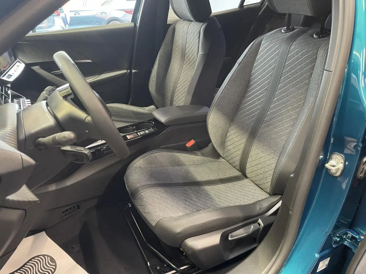 Vue intérieure côté conducteur du Peugeot 2008 bleu, mettant en valeur le siège tissu gris et la console centrale noire brillante.