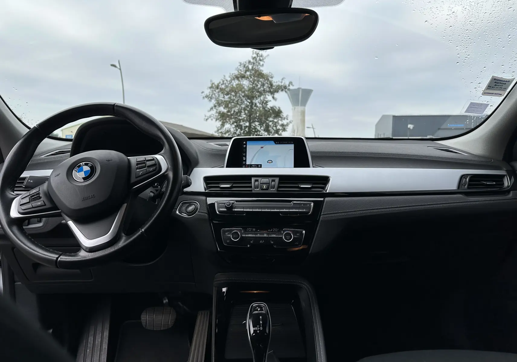 Vue intérieure avant du tableau de bord et volant noir d'une BMW X2 gris 2018 avec écran central et levier de boîte automatique.