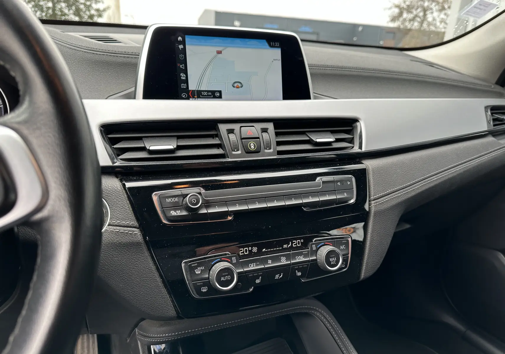 Vue rapprochée du tableau de bord noir du BMW X2 gris 2018, mettant en valeur l'écran GPS et la console de climatisation digitale.