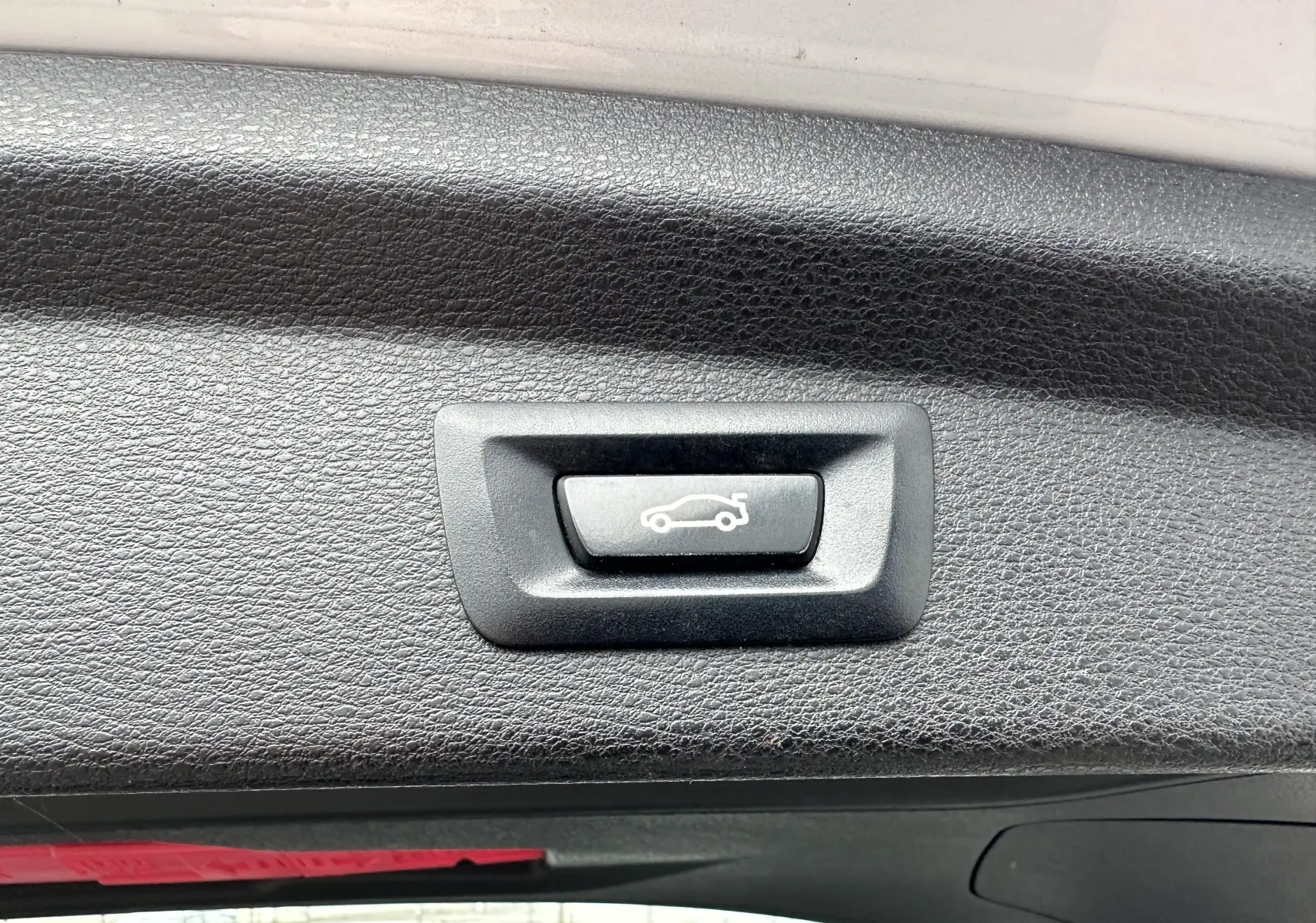 Bouton de déverrouillage du hayon sur la garniture intérieure noire du coffre d'un BMW X2 gris 2018.