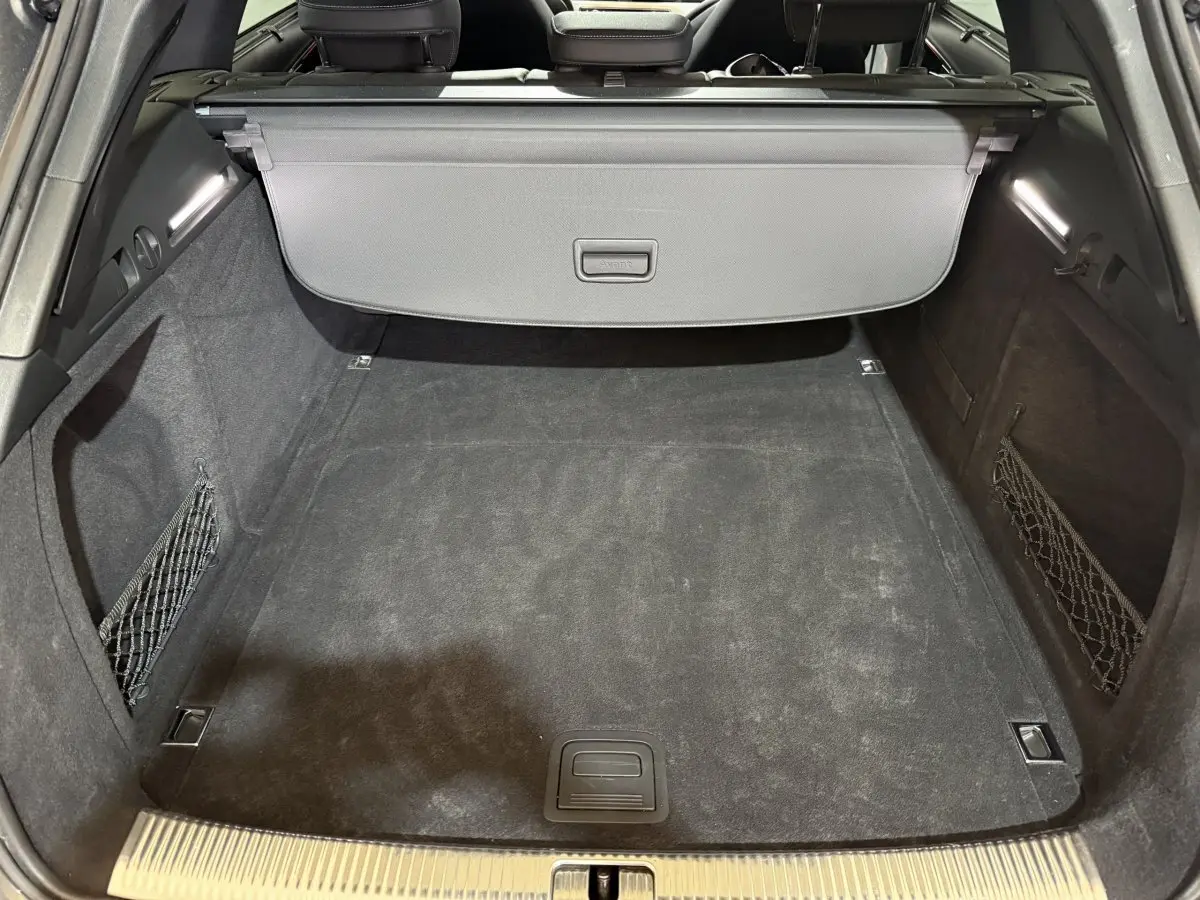 Coffre vu de face, intérieur noir avec filet de rangement latéral, cache-bagages et éclairage LED, Audi A4 gris foncé.