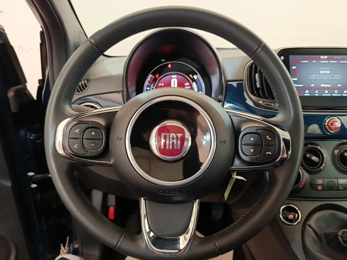 Vue rapprochée du volant en cuir noir avec logo FIAT, tableau de bord et écran tactile bleu de la Fiat 500 Hybrid 2022.
