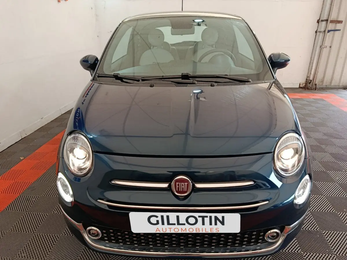 Vue avant d'une Fiat 500 Dolcevita hybride bleu foncé avec phares allumés dans un garage.