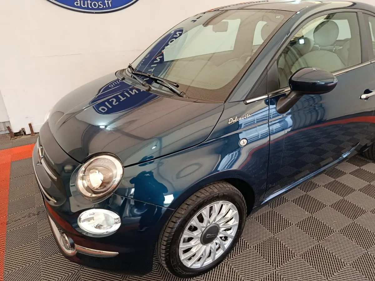 Vue 3/4 avant droite d'une FIAT 500 Dolcevita bleu foncé avec jantes alliage et logo distinctif sur la porte.