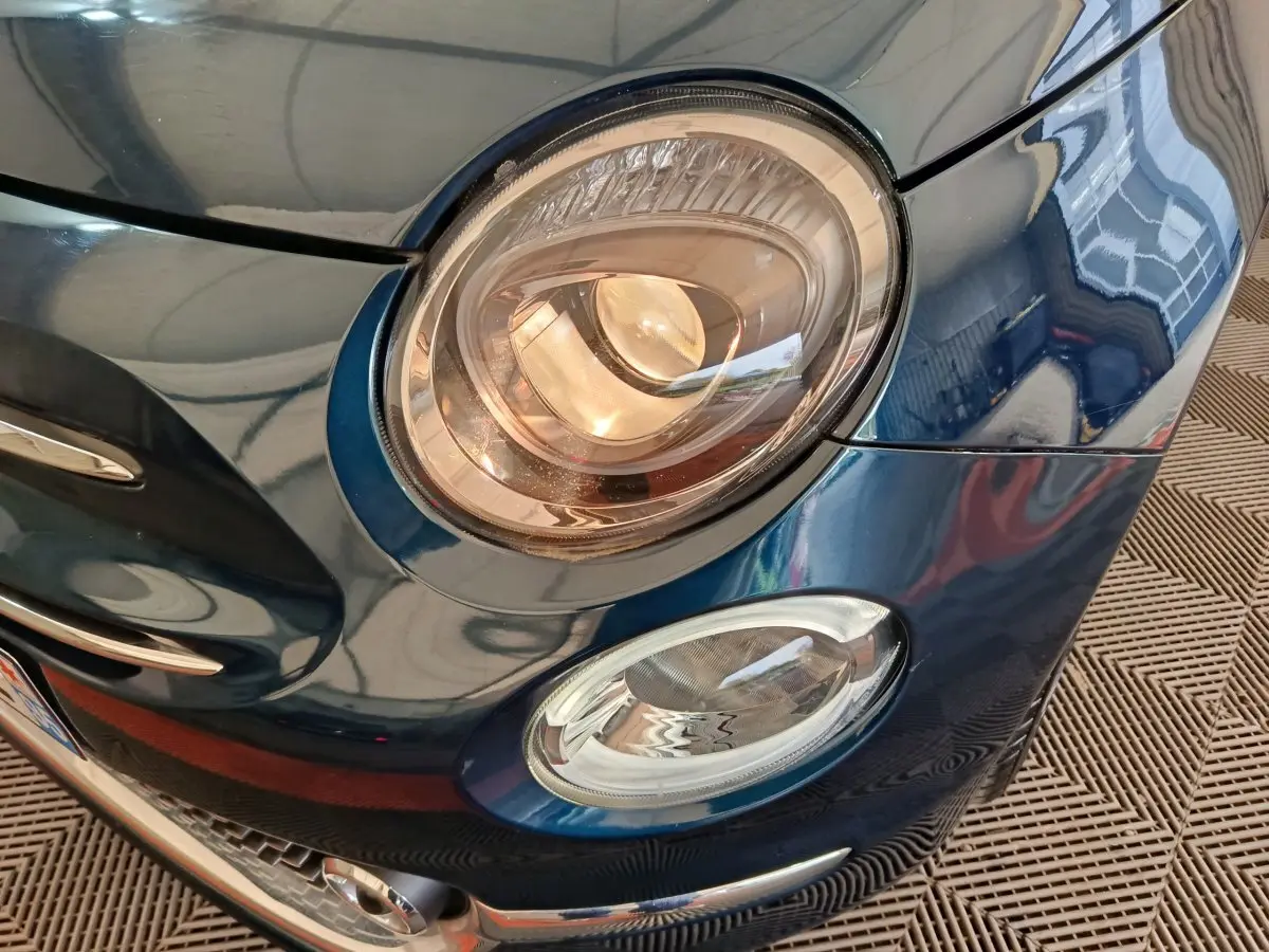 Gros plan sur le phare avant droit bleu métallisé de la Fiat 500 Hybrid Dolcevita 2022 avec détails chromés.