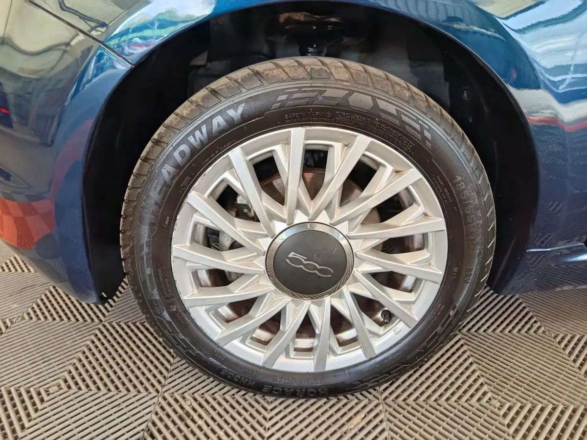Gros plan sur la roue avant droite d'une FIAT 500 Dolcevita bleue avec jante argentée à rayons fins.