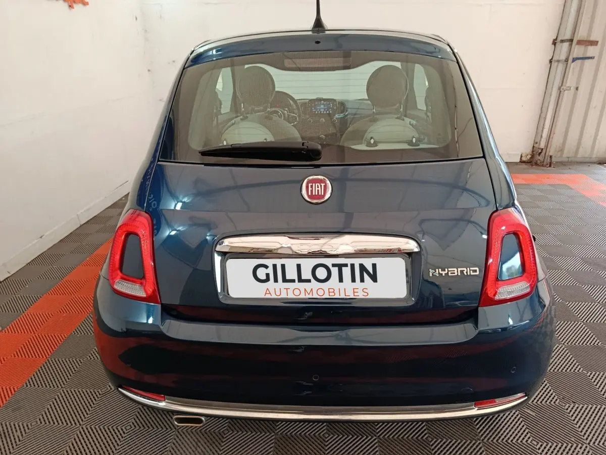 Vue arrière d'une FIAT 500 Hybrid bleu foncé avec feux rouges et logo FIAT visible sur un sol à damier noir et orange.