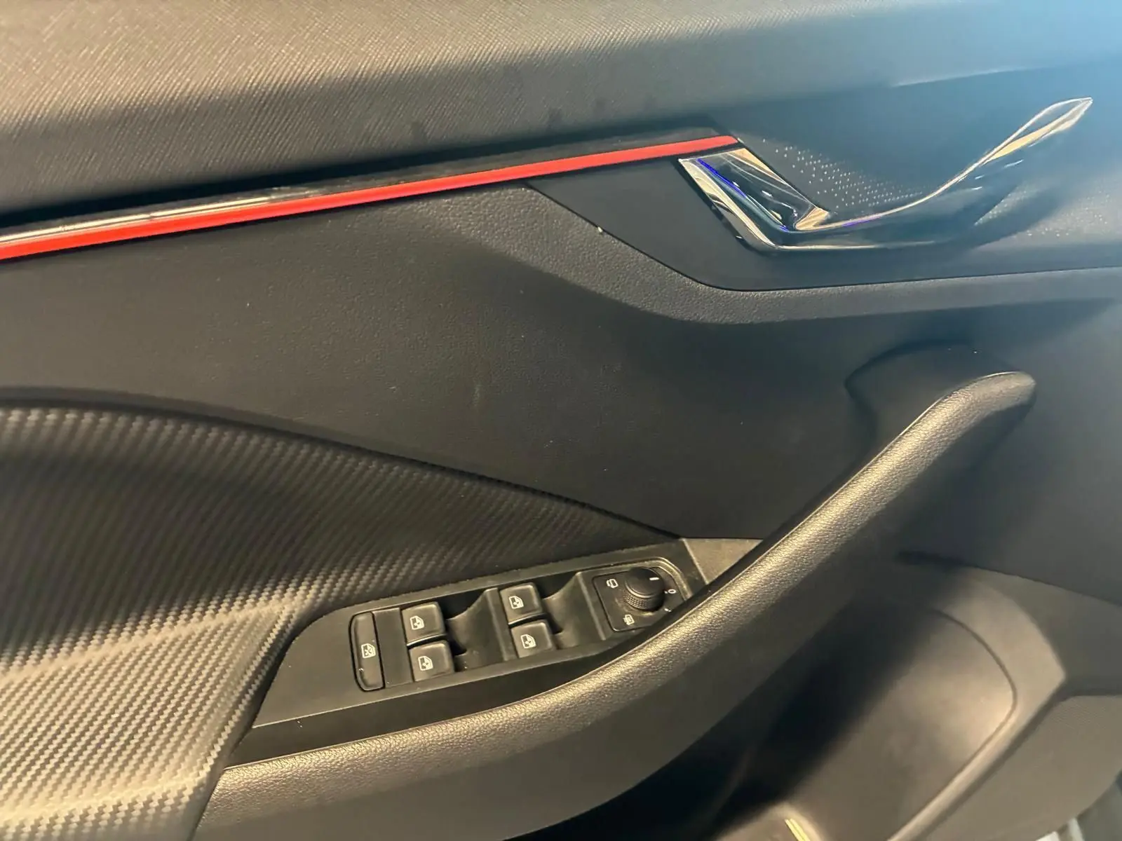 Détail de la porte avant gauche du Skoda Kamiq 2024 gris foncé, avec commandes des vitres et bande décorative rouge.