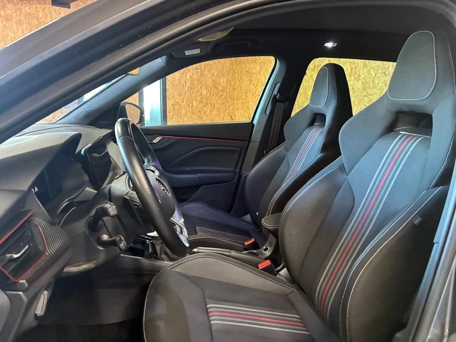 Vue intérieure côté conducteur du Skoda Kamiq 2024 gris foncé, mettant en valeur les sièges sport noirs avec bandes rouges et blanches.