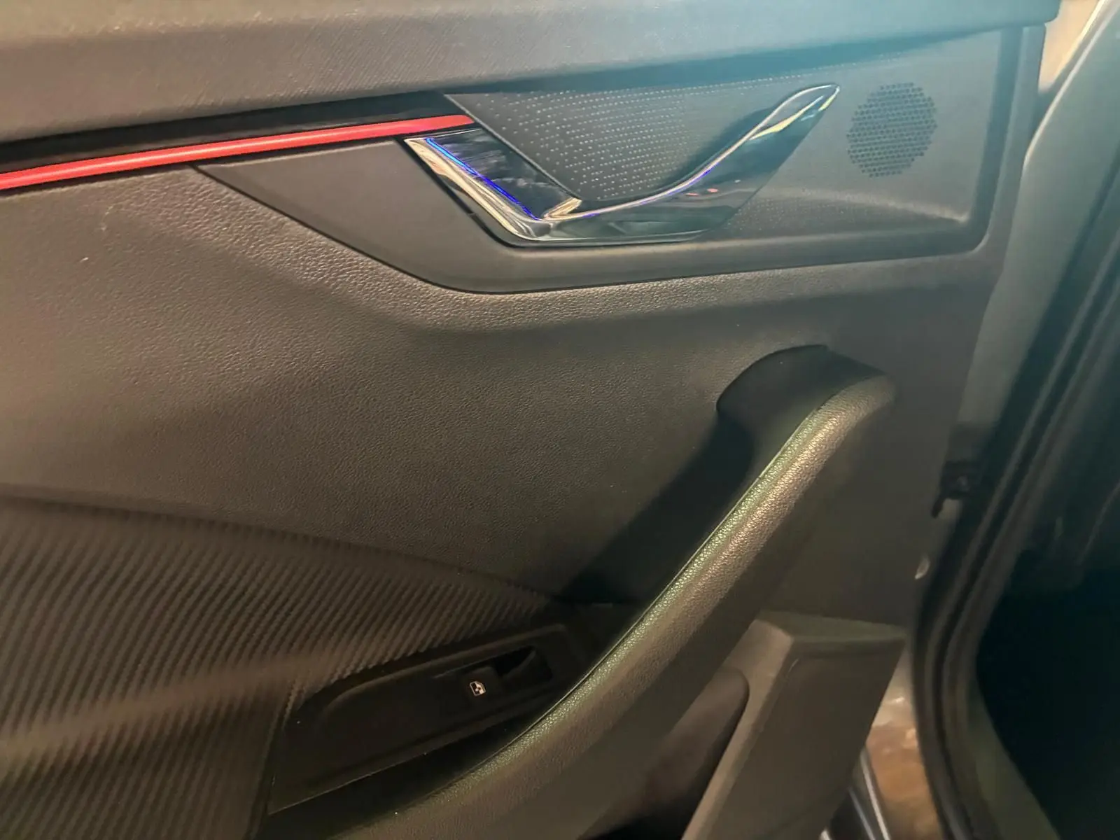 Détail de la porte côté gauche intérieure du Skoda Kamiq 2024 finition Monte-Carlo avec insert rouge et poignée chromée.