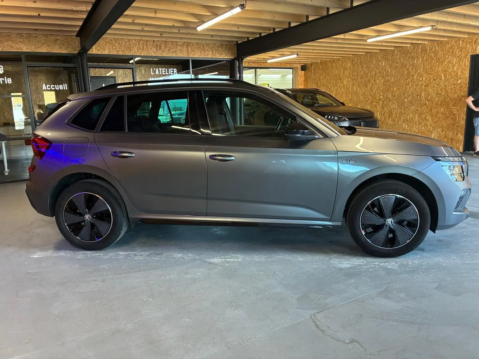 Vue de profil côté gauche d'un Skoda Kamiq gris foncé 2024 finition Monte-Carlo avec jantes noires distinctives.