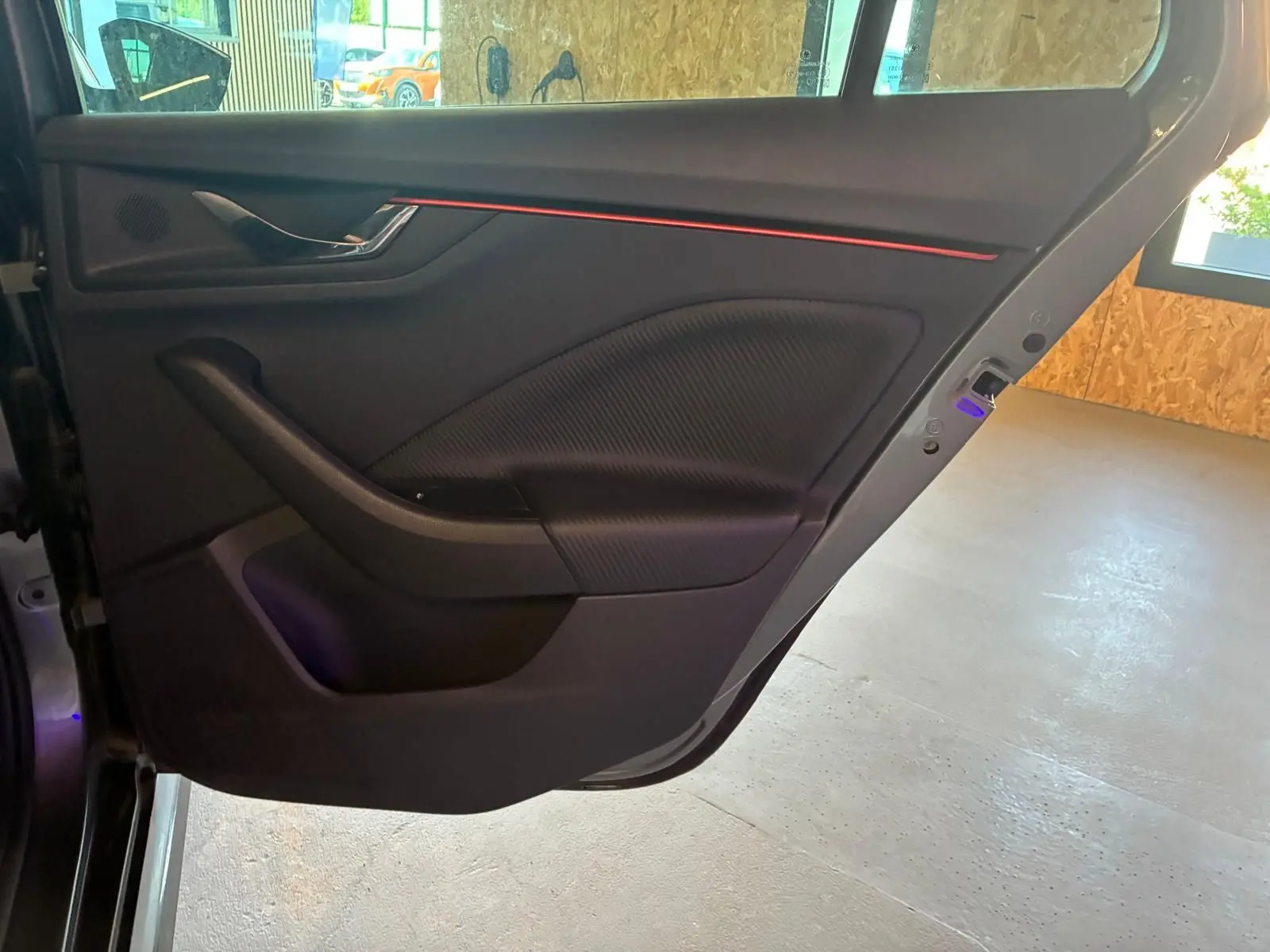 Intérieur de la porte arrière gauche du Skoda Kamiq 2024 gris foncé, avec bande lumineuse rouge et finition texturée.