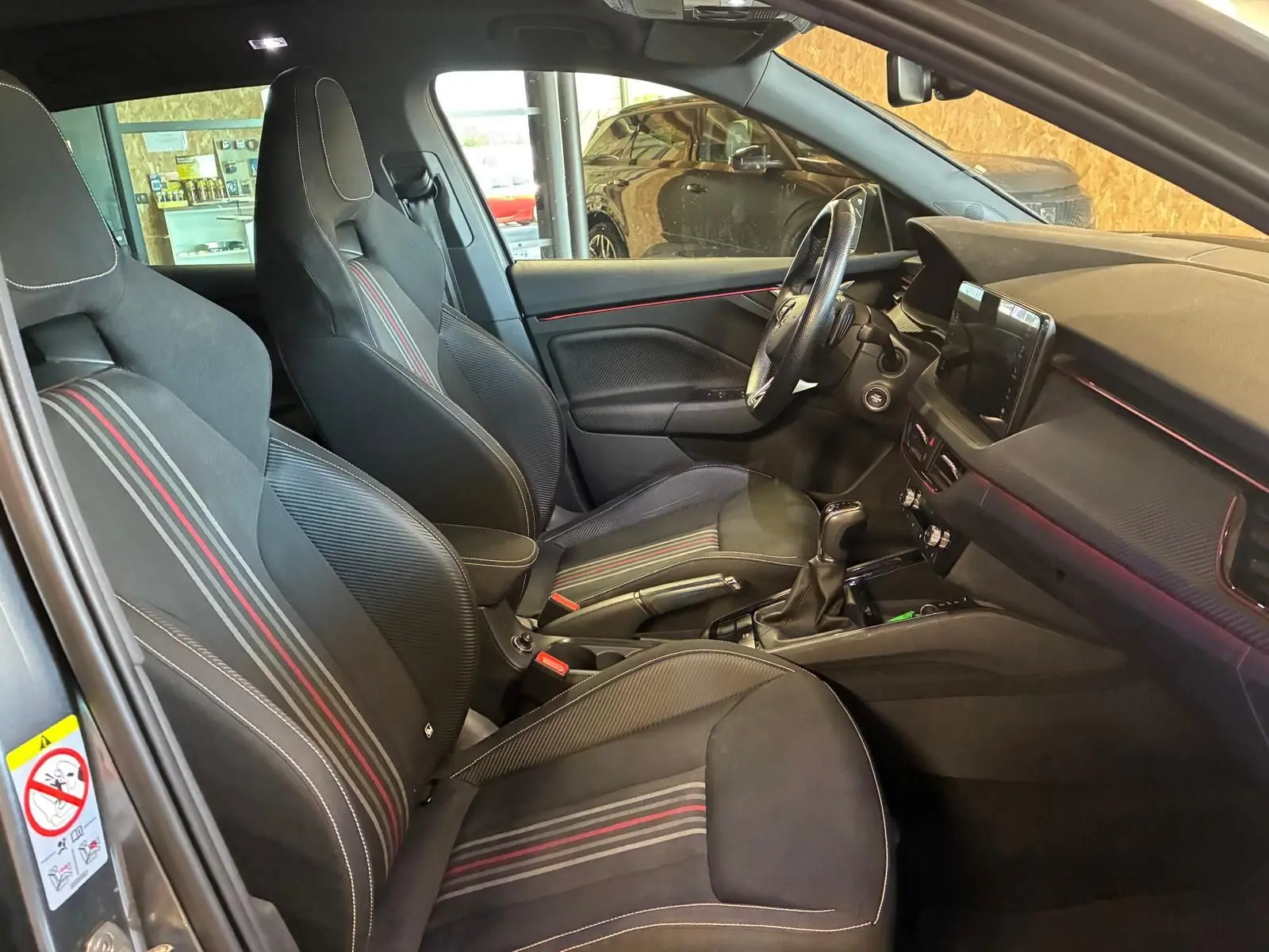 Intérieur de la Skoda Kamiq 2024 en vue latérale gauche, sièges tissu noir avec bandes rouges et tableau de bord moderne.