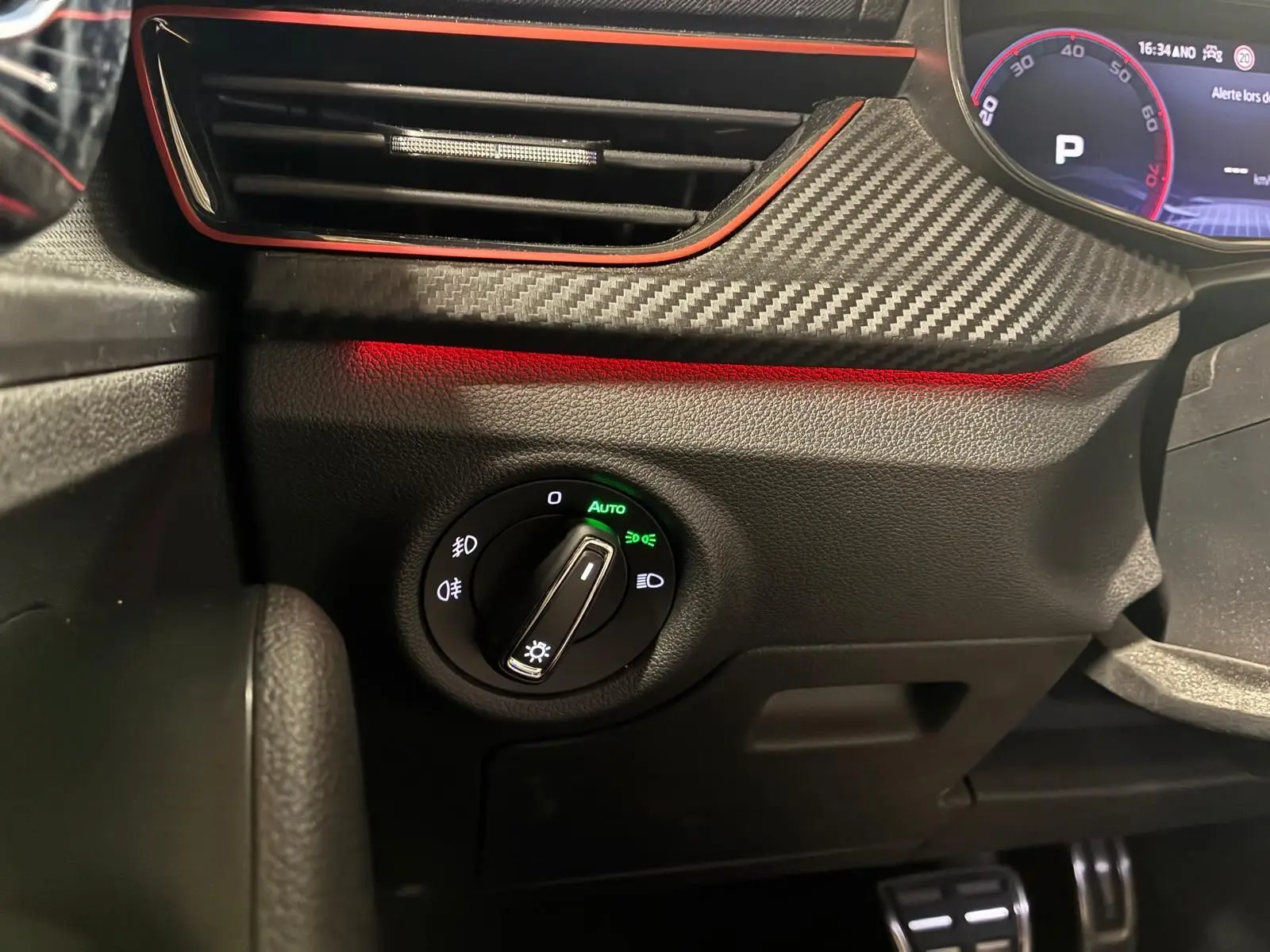 Gros plan sur le bouton de commande des phares avec éclairage vert, tableau de bord noir et insert effet carbone du Skoda Kamiq 2024.