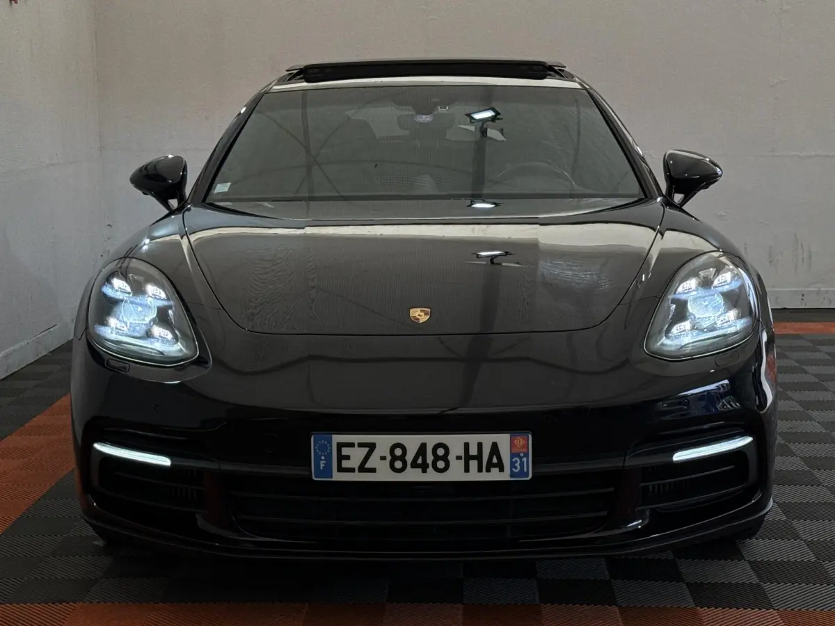 Vue frontale d'une Porsche Panamera 4 E-Hybrid Sport Turismo noire avec phares LED allumés et plaque d'immatriculation française.