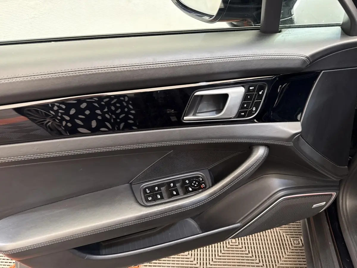 Vue intérieure côté gauche de la porte avant noire de la Porsche Panamera 4 E-Hybrid avec commandes électriques et finition cuir.