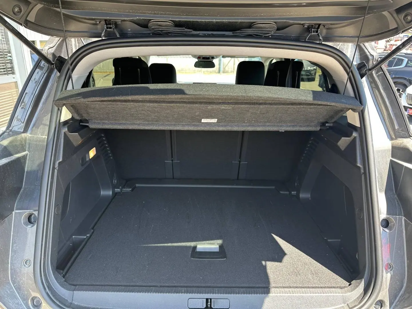 Coffre ouvert vu de l'arrière d'un Citroën C5 Aircross gris Platinium, avec cache-bagages relevé et intérieur noir.