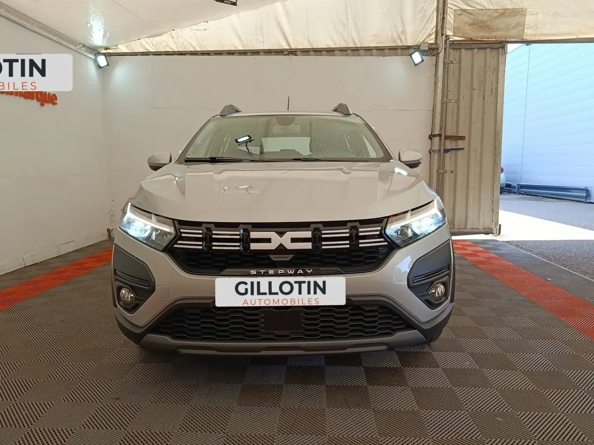 Vue frontale d'une Dacia Sandero Expression gris clair avec phares LED allumés dans un garage.