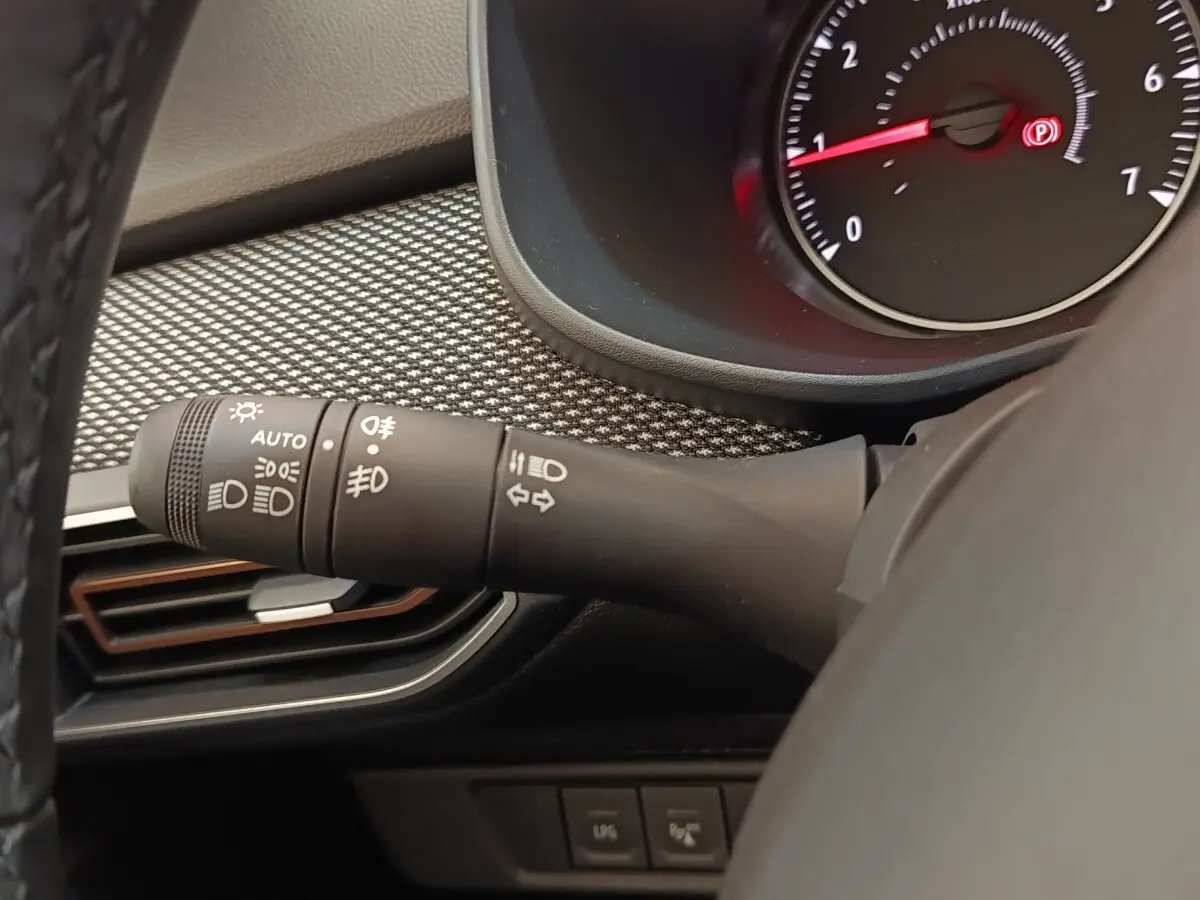 Gros plan sur la manette des feux à gauche du volant cuir synthétique dans l’habitacle gris clair du Dacia Sandero 2023.