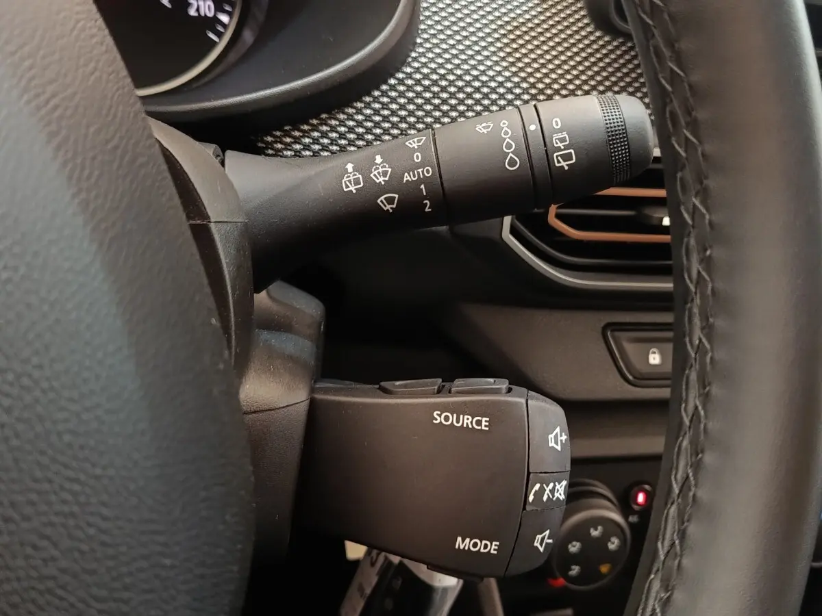 Gros plan sur la commande multifonctions à gauche du volant cuir noir dans l’habitacle d’une Dacia Sandero gris clair 2023.