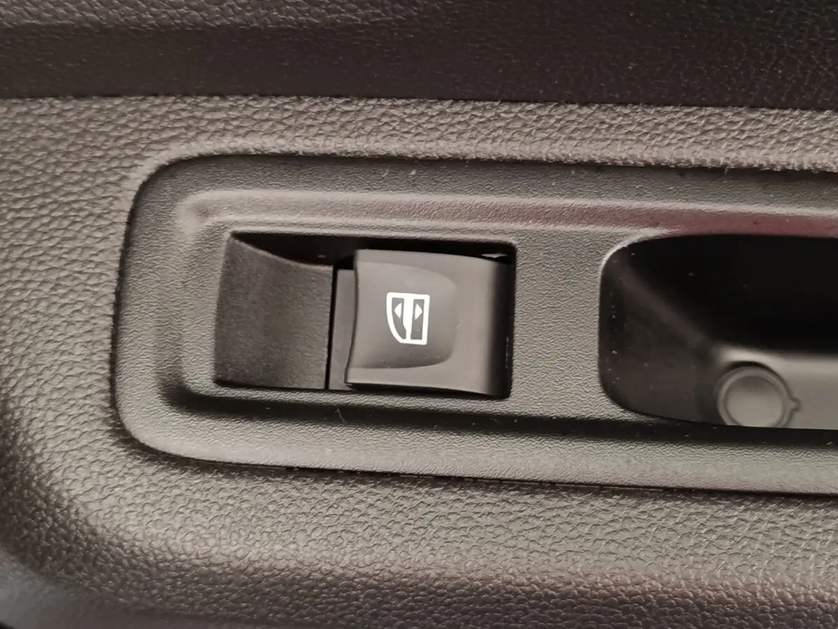 Gros plan sur le bouton de commande électrique de la fenêtre côté conducteur dans l’habitacle noir de la Dacia Sandero gris clair.