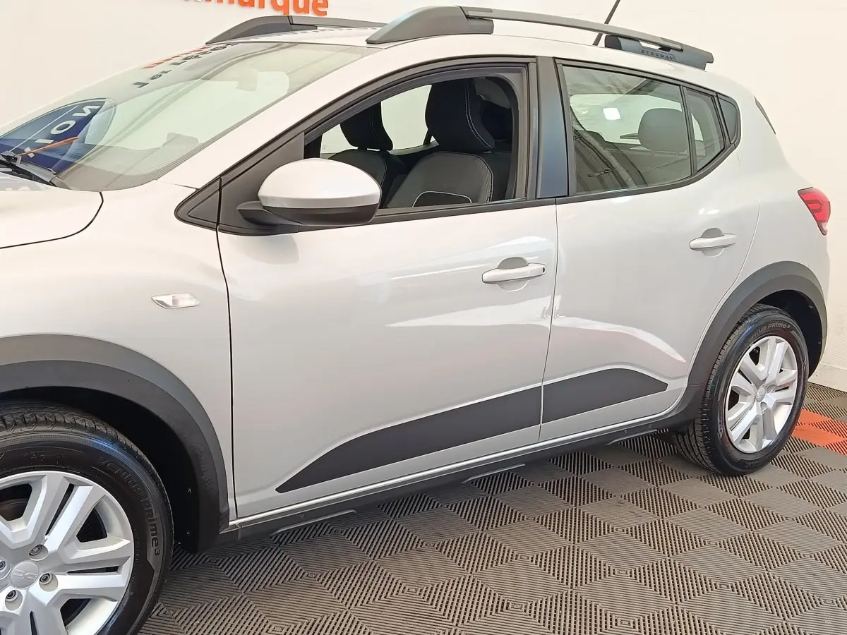 Vue latérale droite d'une Dacia Sandero Expression gris clair avec protections noires et jantes argentées.