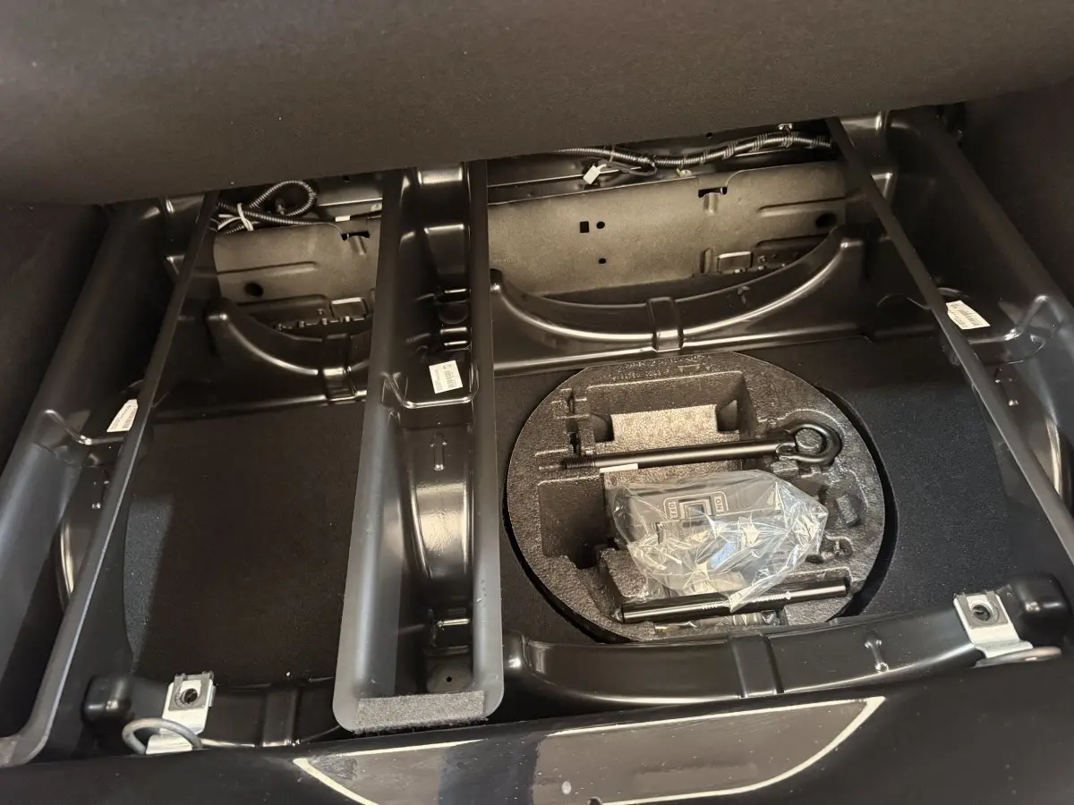 Vue intérieure du coffre de la Renault ZOE noire 2024, montrant le rangement sous plancher avec outils et espace de chargement.
