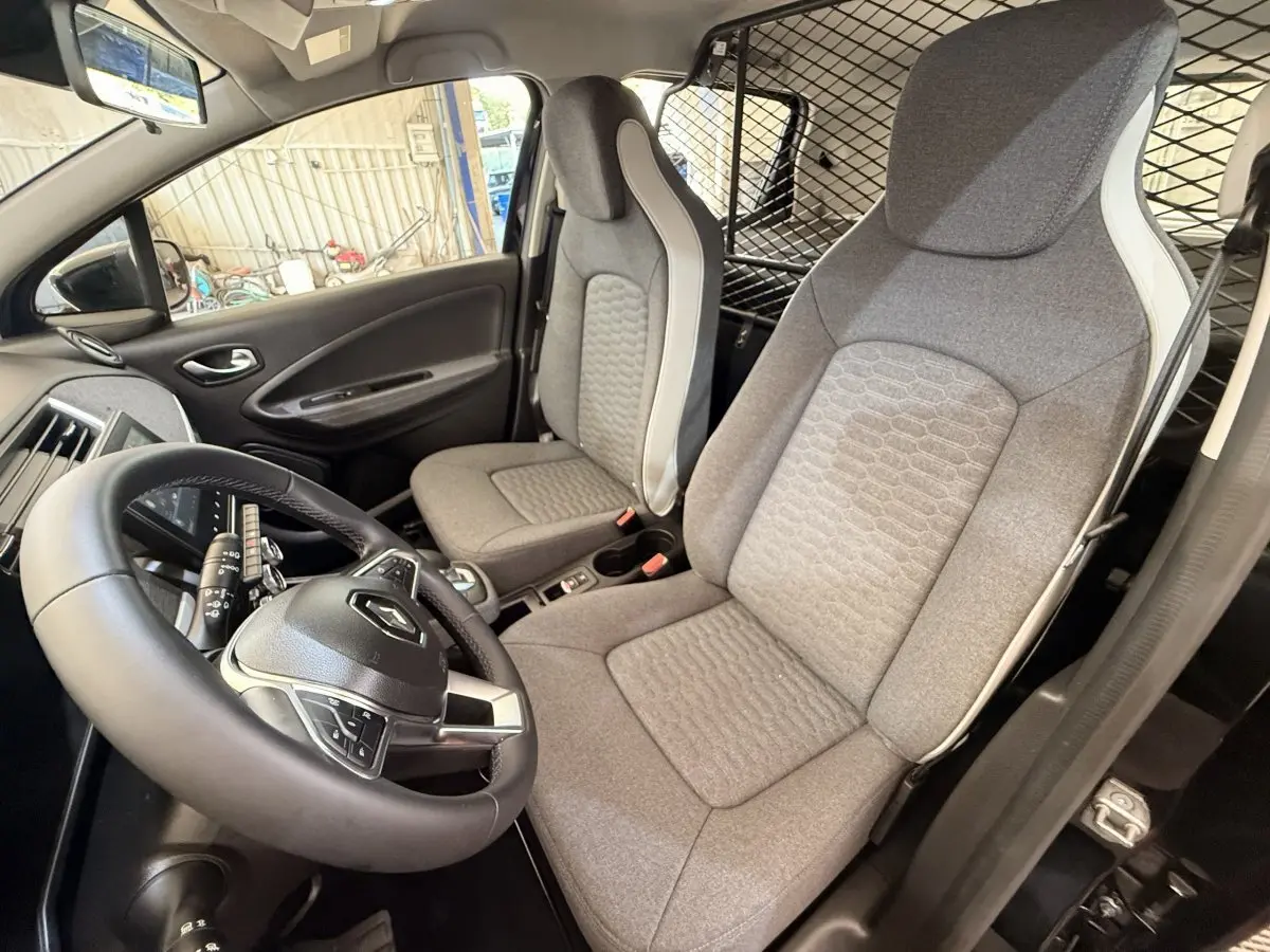 Vue intérieure côté conducteur de la Renault ZOE noire 2024, volant cuir synthétique et sièges gris avec séparation grillagée.