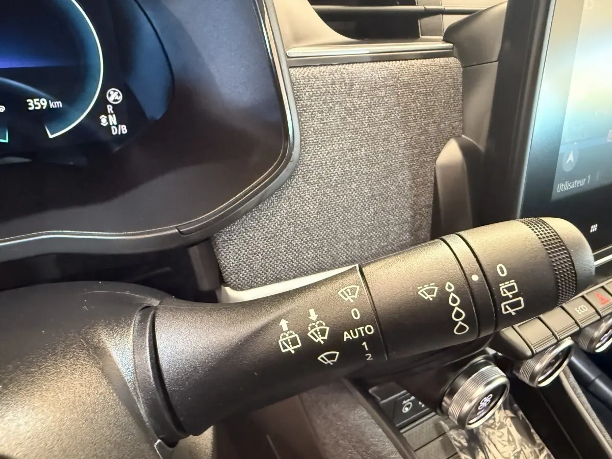 Gros plan sur la commande des essuie-glaces dans l'habitacle de la Renault ZOE noire, avec tableau de bord numérique visible.