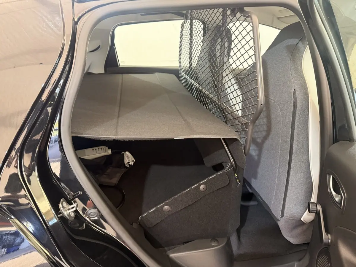 Vue intérieure arrière côté droit de la Renault ZOE noire 2024 avec séparation grillagée et banquette rabattue.