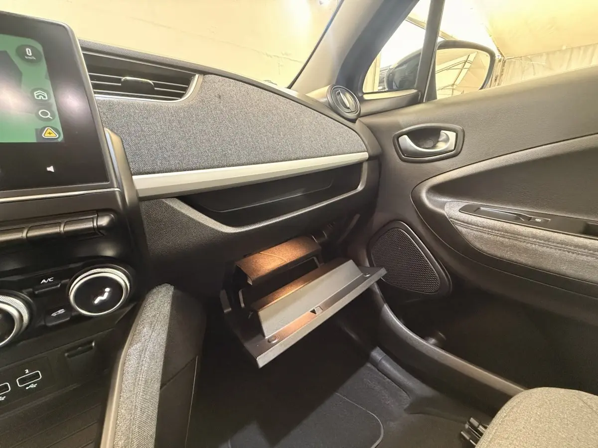 Intérieur Renault ZOE noir, vue côté passager avec boîte à gants ouverte et tableau de bord gris texturé.