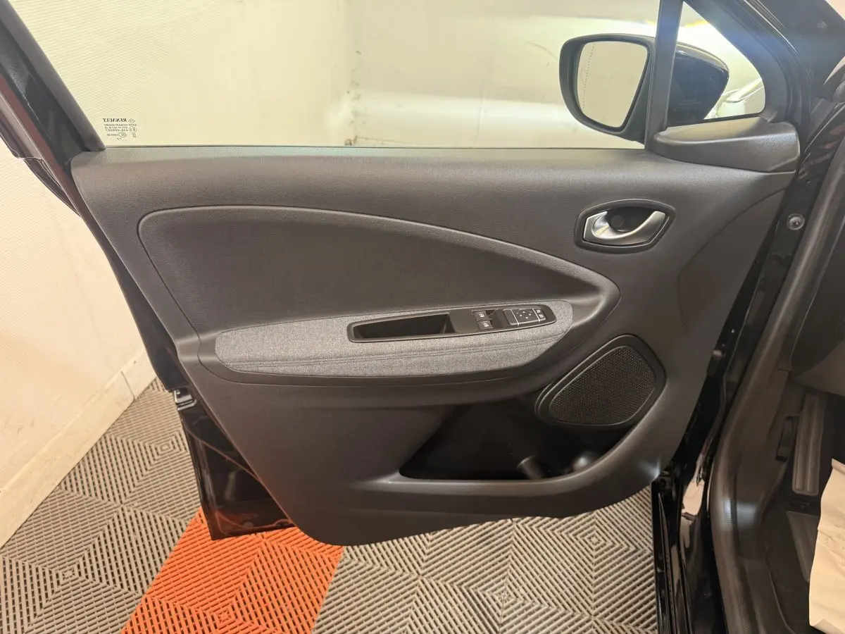 Vue intérieure de la porte avant gauche noire de la Renault ZOE 2024 avec accoudoir tissu gris et commandes électriques.