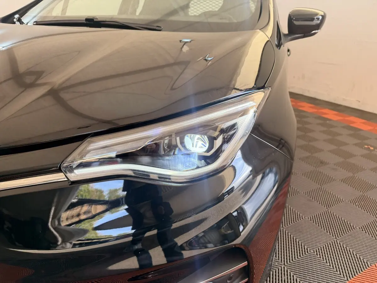 Gros plan sur le phare avant droit d'une Renault ZOE noire 2024, avec reflet brillant sur la carrosserie.
