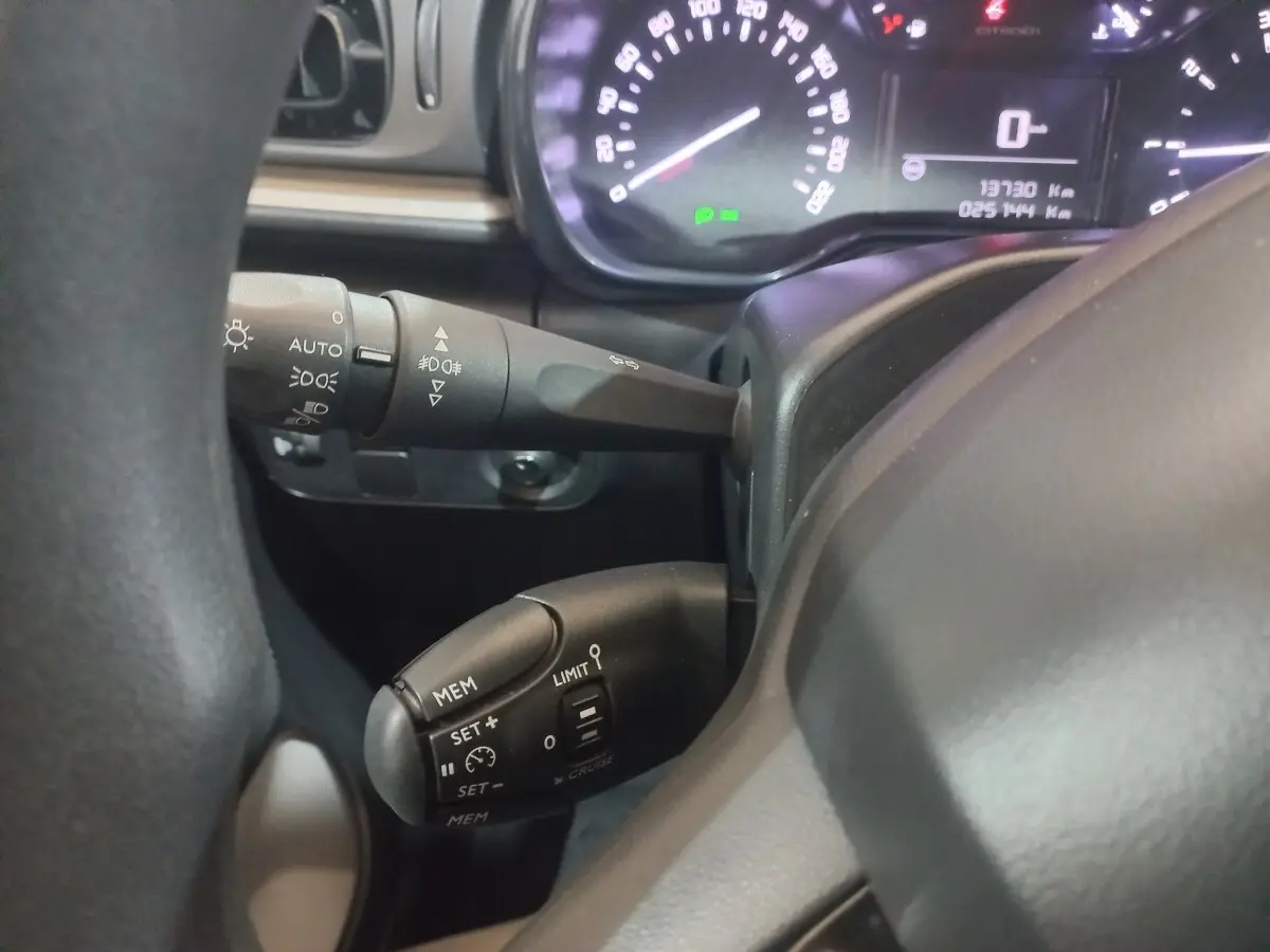 Gros plan sur le volant noir de la Citroën C3 2024, montrant les commandes de régulateur de vitesse et les leviers de clignotants.