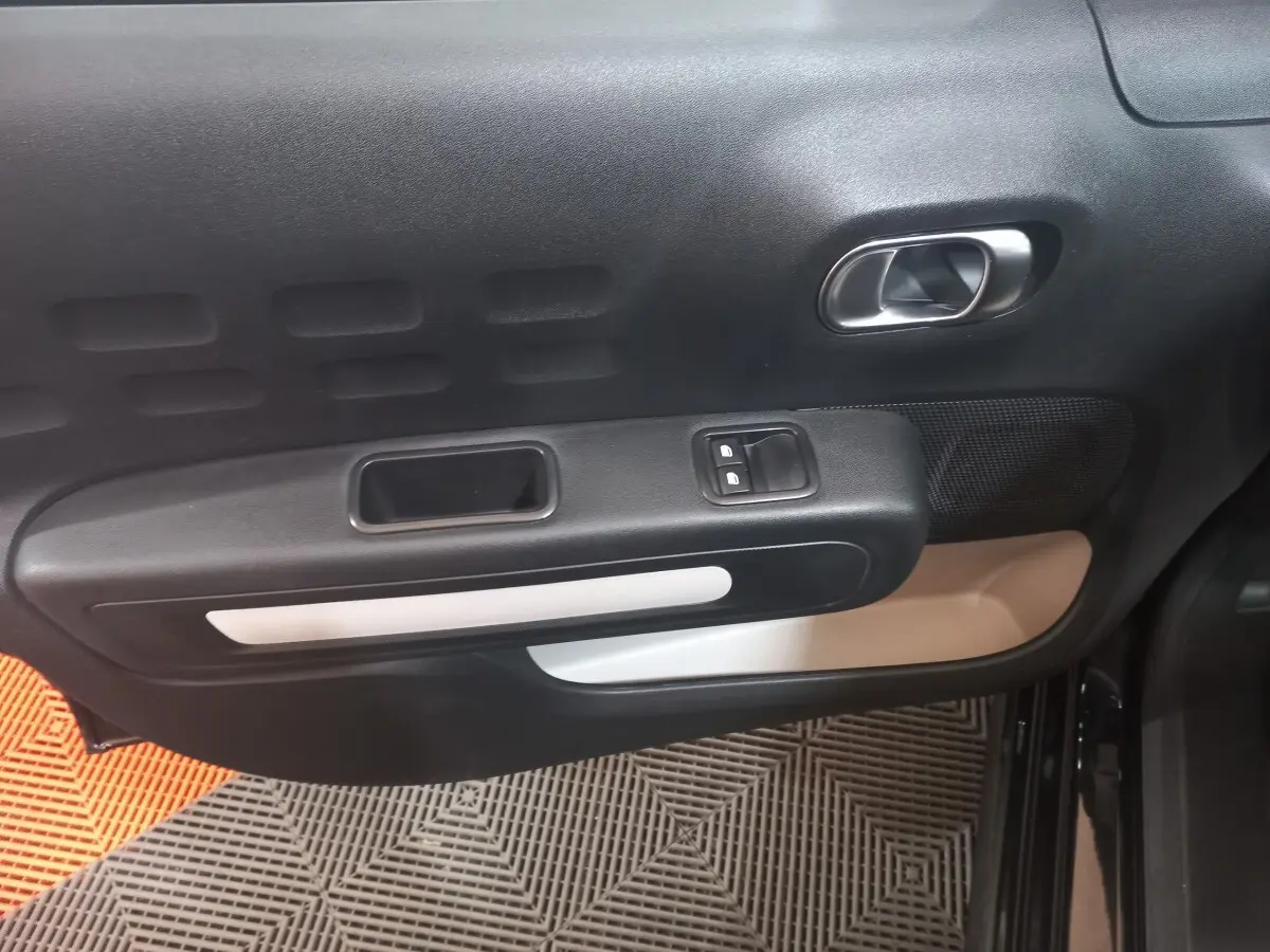 Vue intérieure du panneau de porte avant gauche noir de la Citroën C3 2024 avec commandes de vitres et poignée argentée.