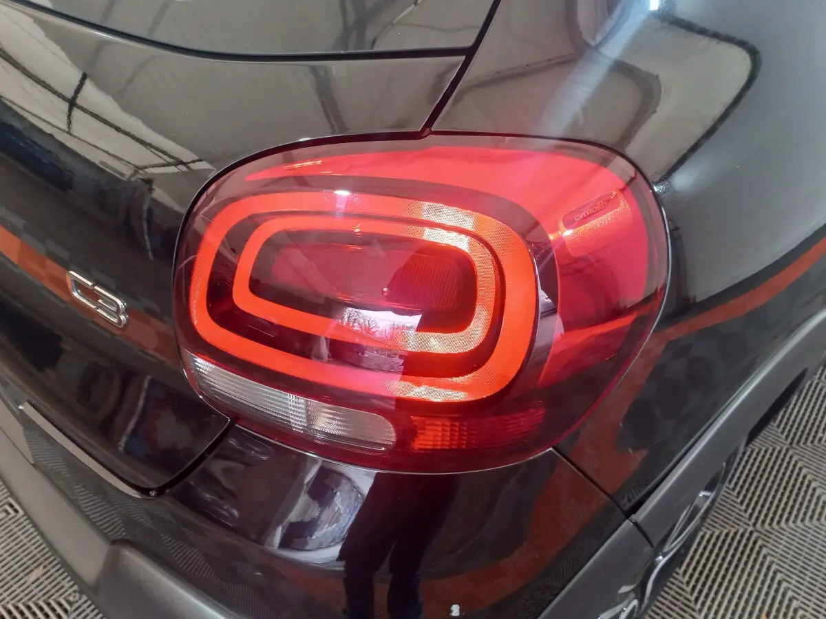 Gros plan sur le feu arrière droit rouge d’une Citroën C3 noire, avec le logo C3 visible sur la carrosserie.
