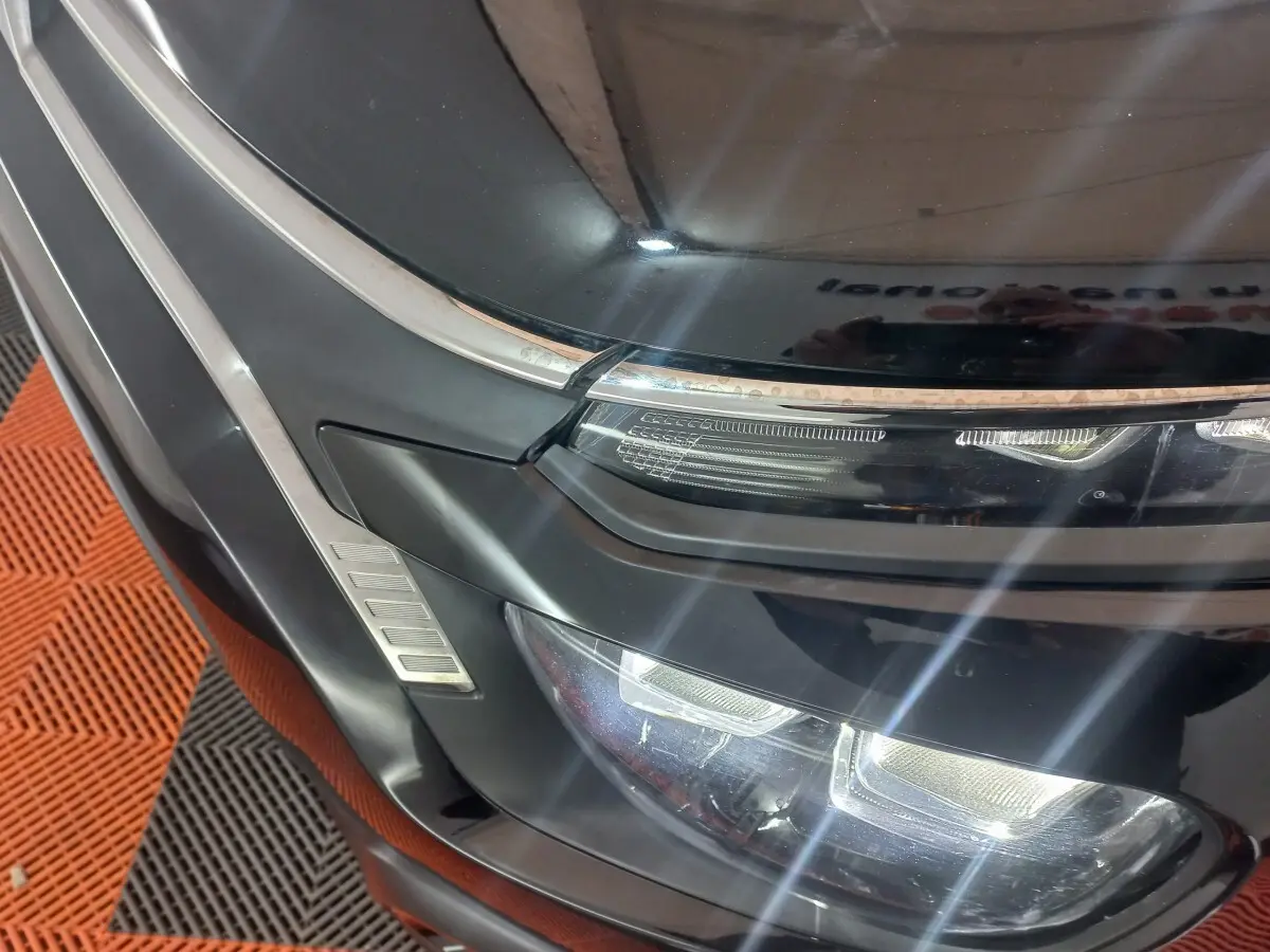 Gros plan sur le phare avant droit noir brillant de la Citroën C3 2024 avec détails chromés et éclairage LED allumé.