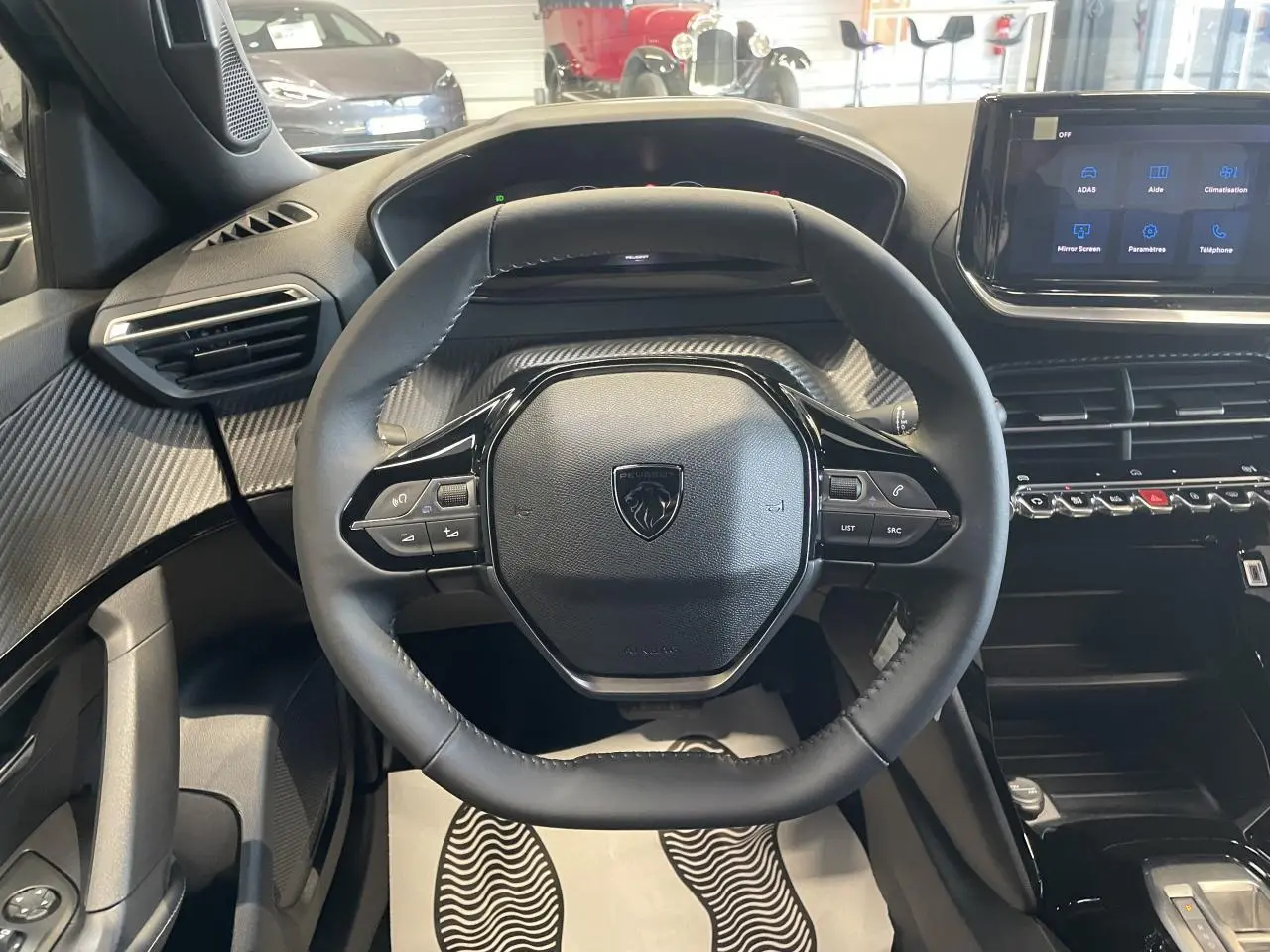 Vue centrée sur le volant compact Peugeot 2008 avec tableau de bord et écran tactile, intérieur noir et décor carbone.