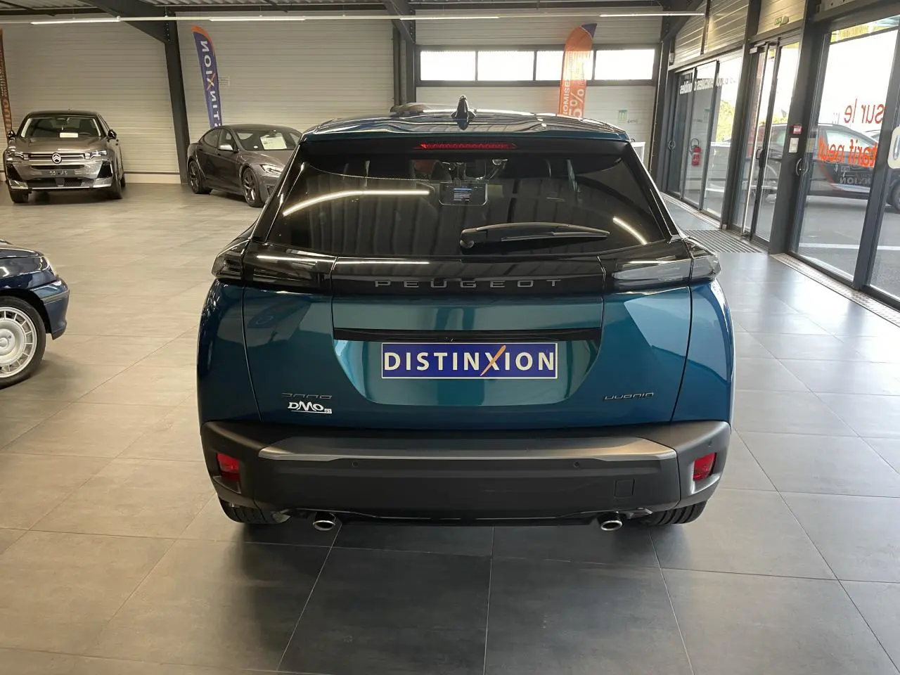 Vue arrière d'un Peugeot 2008 bleu métallisé en showroom avec feux arrière à LED et double sortie d'échappement chromée.