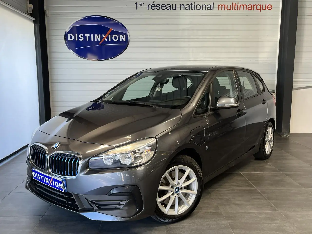 BMW Série 2 225xe Active Tourer gris vue 3/4 avant droit en intérieur avec jantes alliage et calandre chromée.