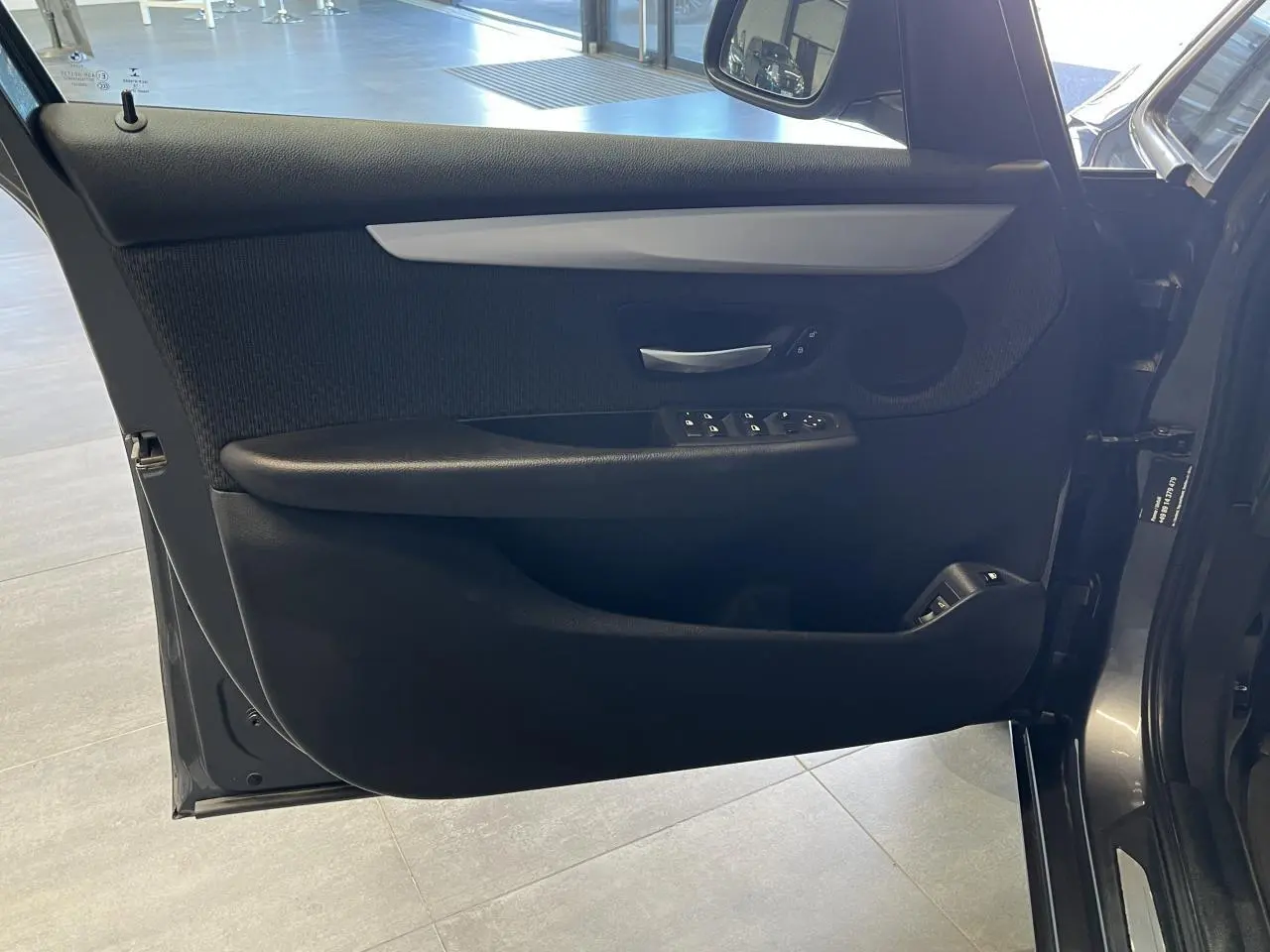 Gros plan sur la porte côté gauche d'une BMW Série 2 225xe Active Tourer grise, montrant les commandes de vitres et la poignée intérieure.