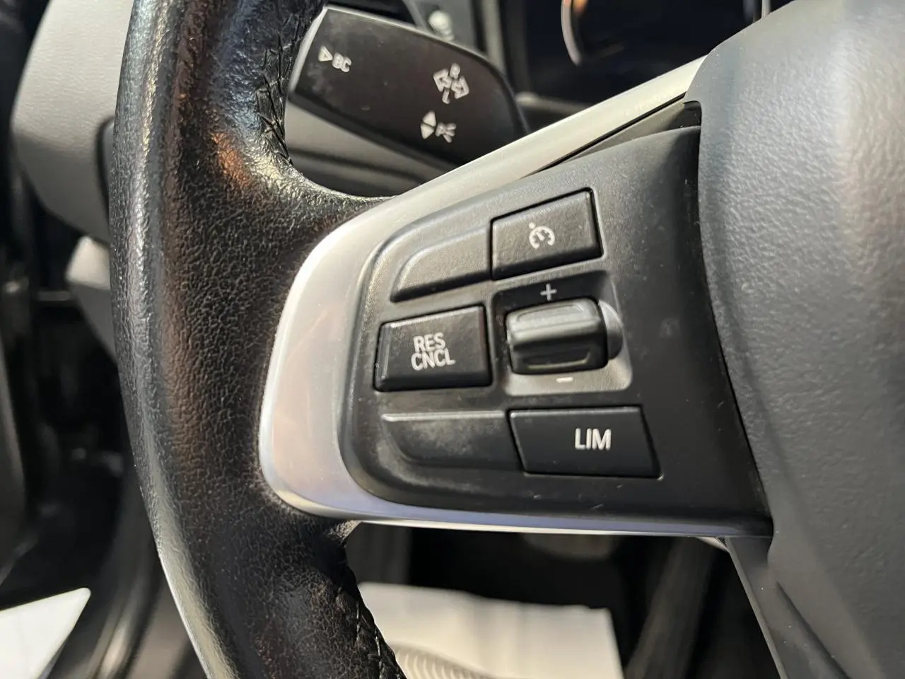 Gros plan sur les commandes de régulateur de vitesse au volant cuir noir d'une BMW Série 2 Active Tourer gris 2018.