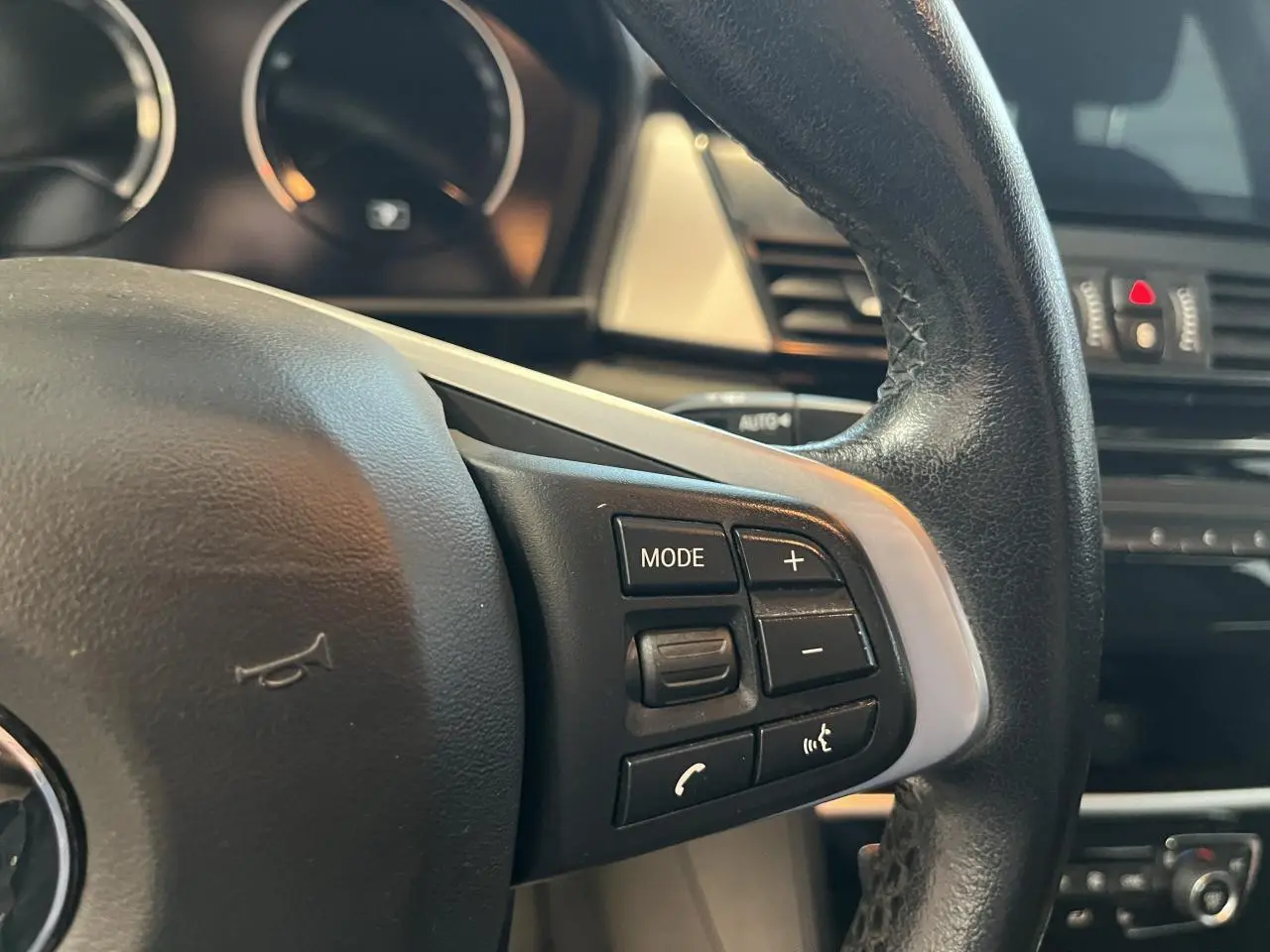 Gros plan sur les commandes du volant cuir noir d'une BMW Série 2 225xe Active Tourer gris, modèle 2018.