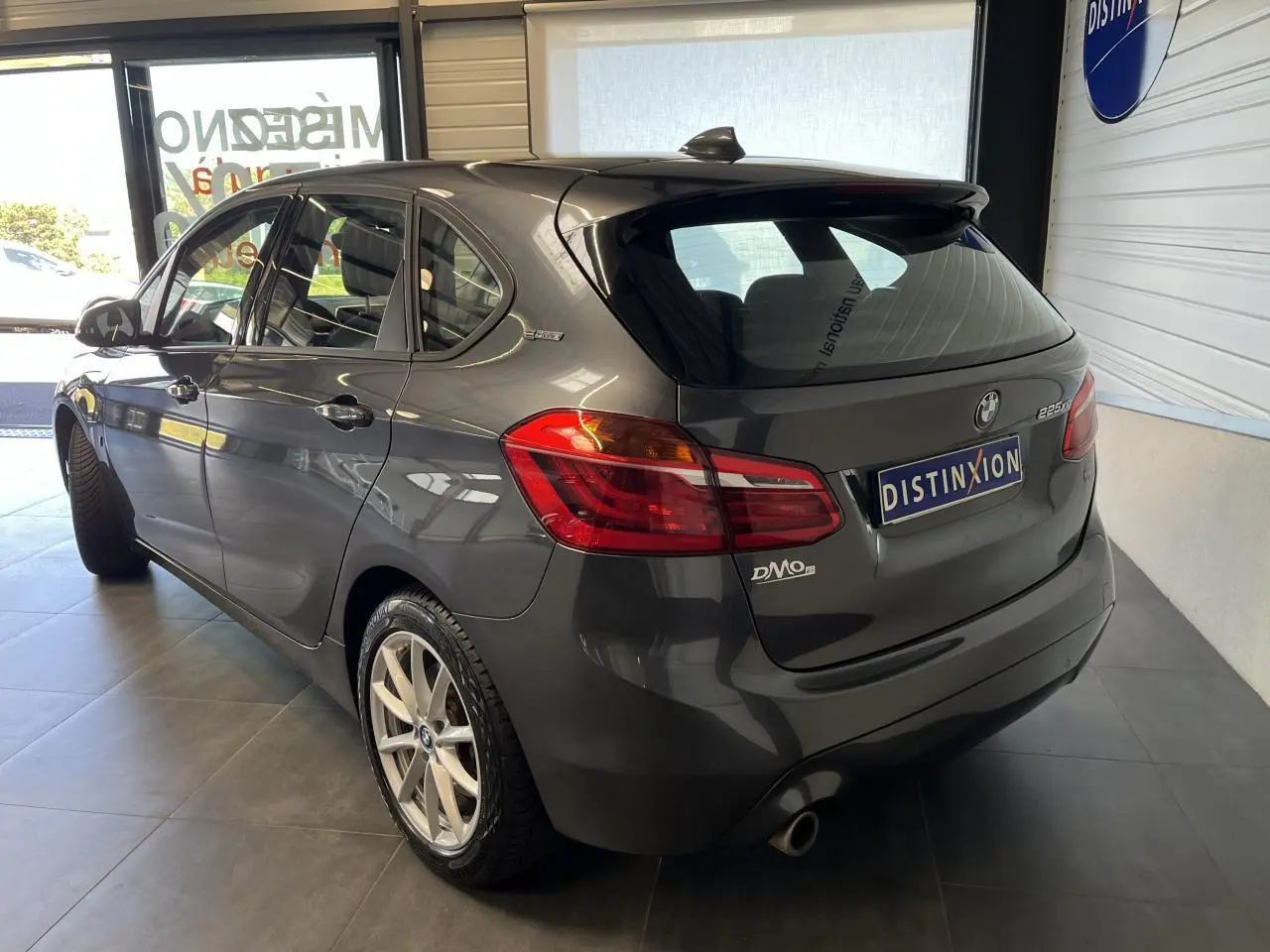 BMW Série 2 225xe Active Tourer gris vue 3/4 arrière droit en intérieur avec jantes argentées et badge hybride.