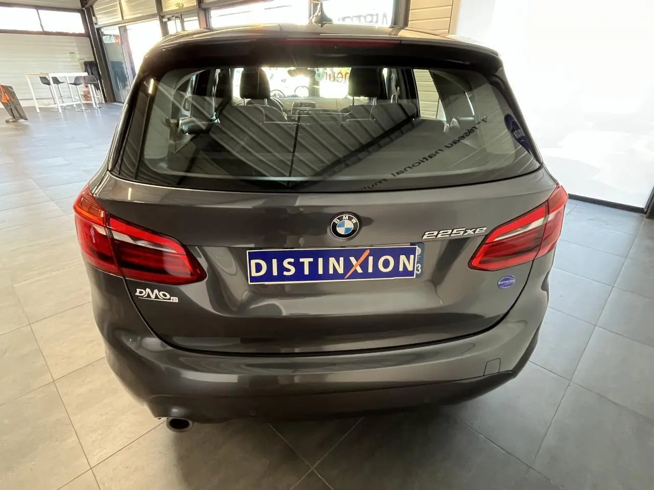 Vue arrière d'une BMW Série 2 225xe Active Tourer grise, avec logo et plaques distinctives visibles en intérieur showroom.