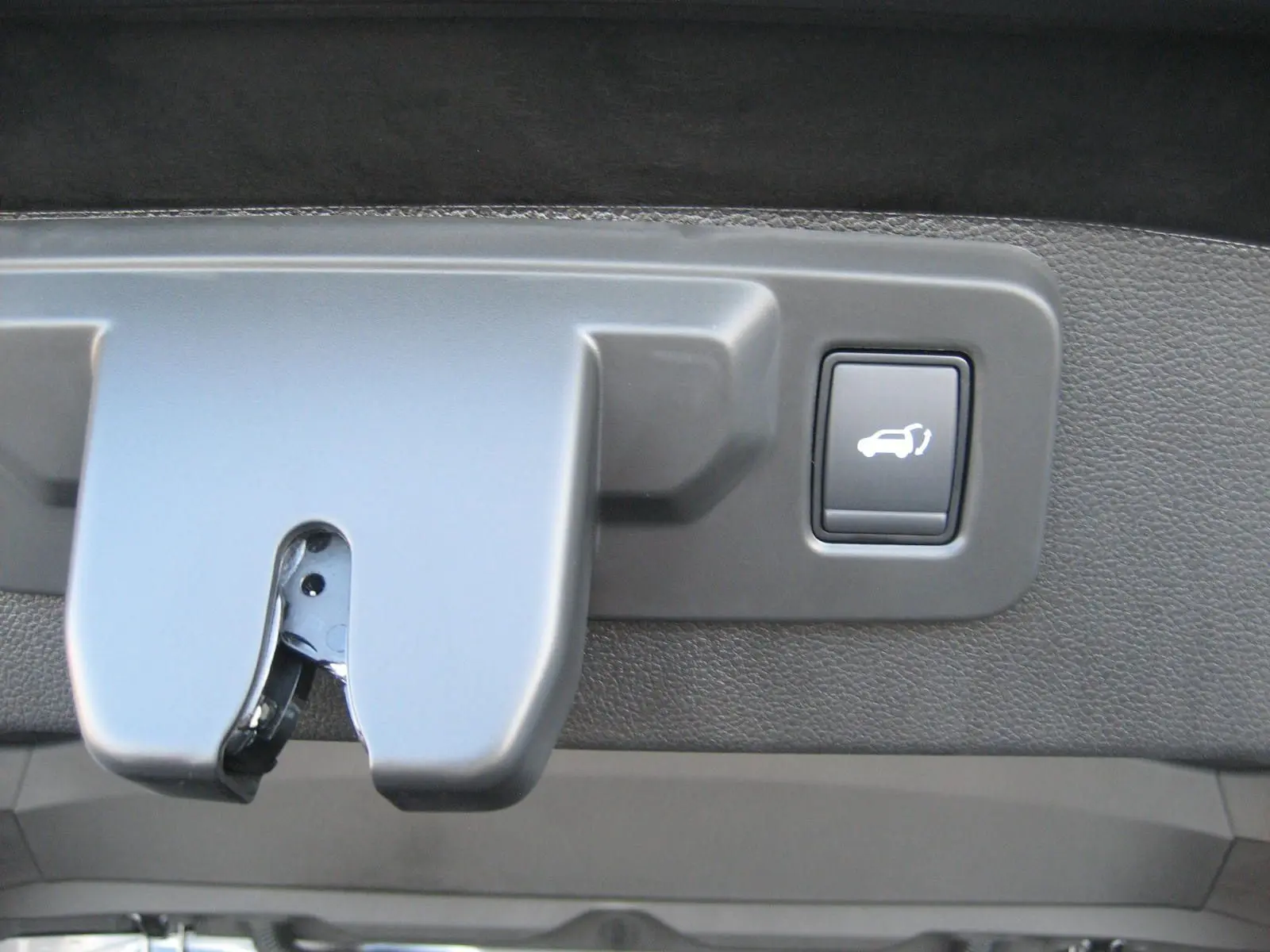 Gros plan sur le bouton d'ouverture électrique du coffre du Renault Austral gris schiste, intérieur du hayon visible.