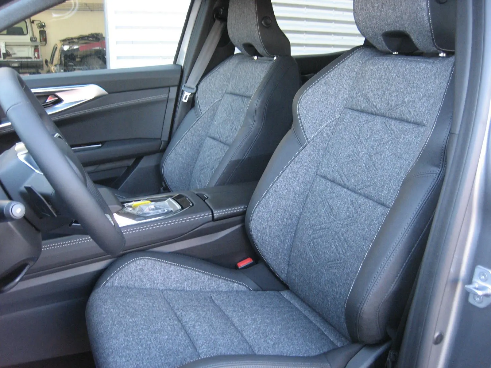 Vue intérieure côté conducteur du Renault Austral 2025, sièges gris tissu avec contours cuir noir et console centrale visible.